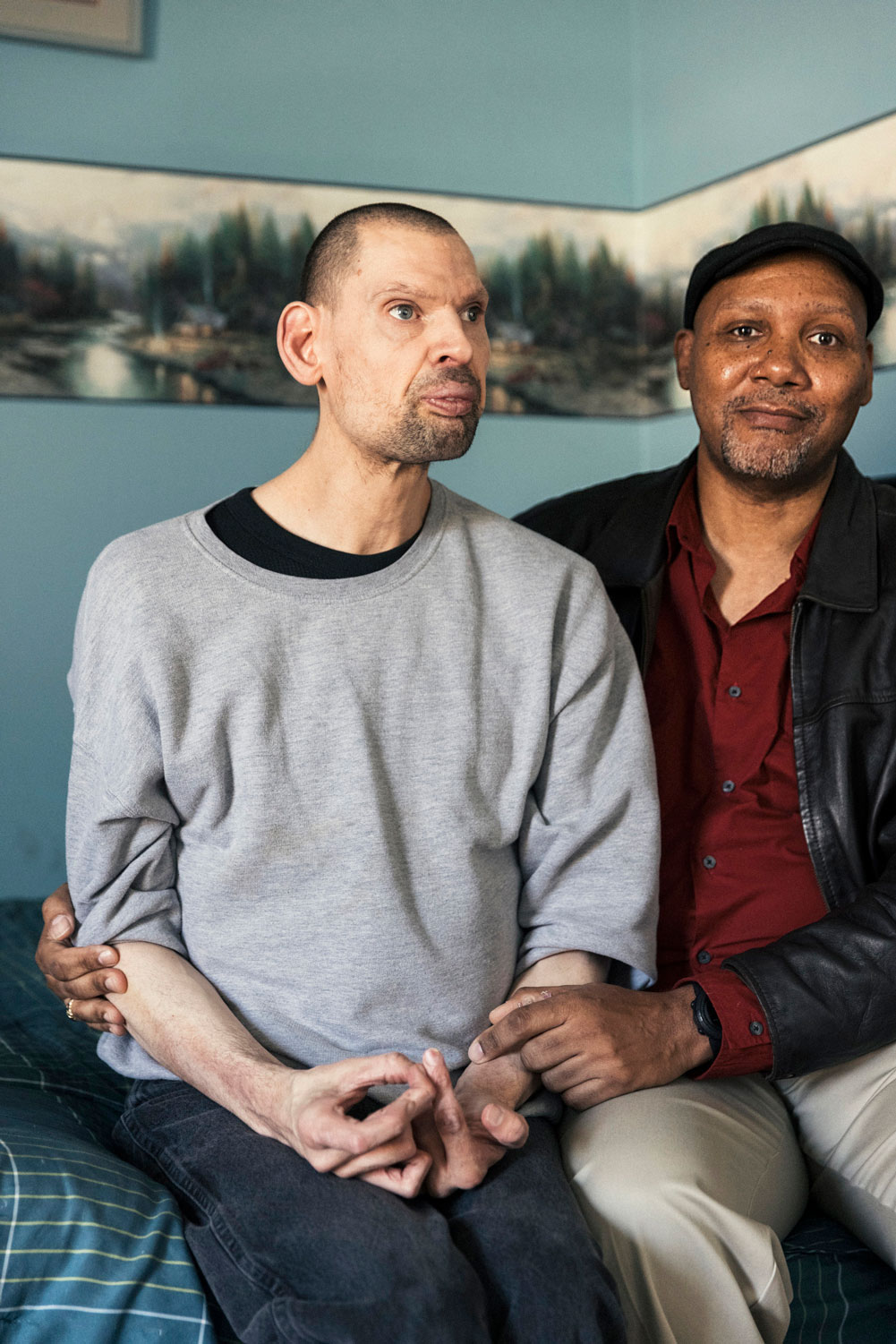 Two people sitting together with the man on the rights arm around the back of the man on the left.