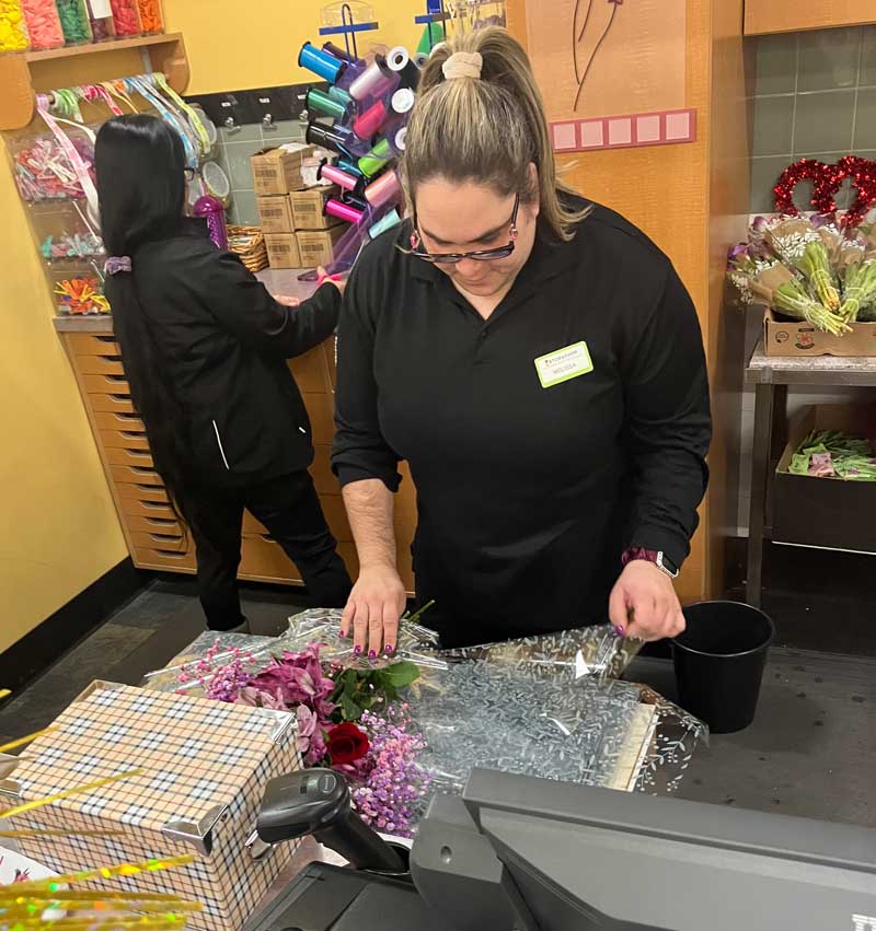 Melissa working at Stop & Shop she is working at a table wrapping cellophane around an arrangement of flowers