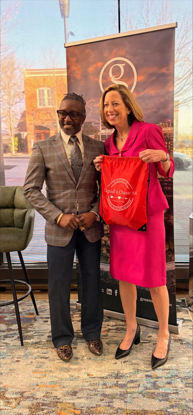 Anthony Thompson stands beside Mayor Pro Tem Dorothy Dowe. Mayor Pro Tem Dowe holds a Cupid’s Chase 5K drawstring bag, one of the races swag items participants will receive.