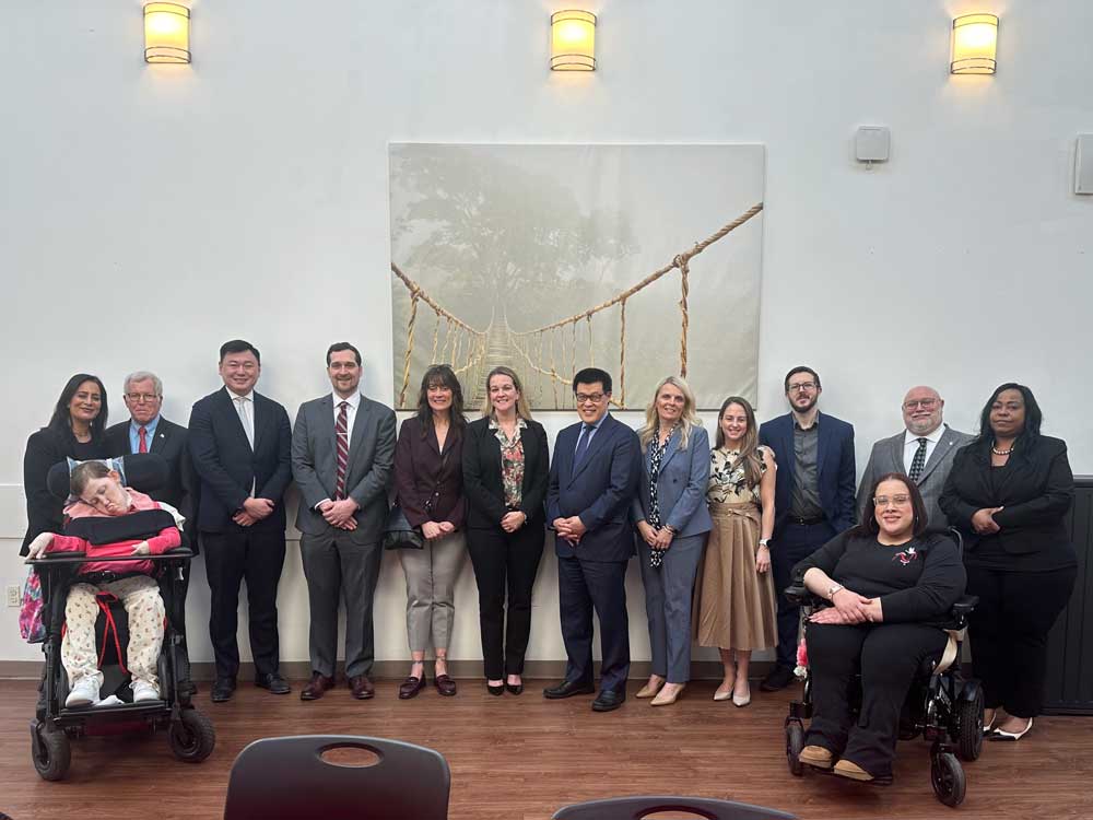 A group of 14 people including visitors employees and program participants posing for a photo inside the Hillsborough Red Ribbon Academy.