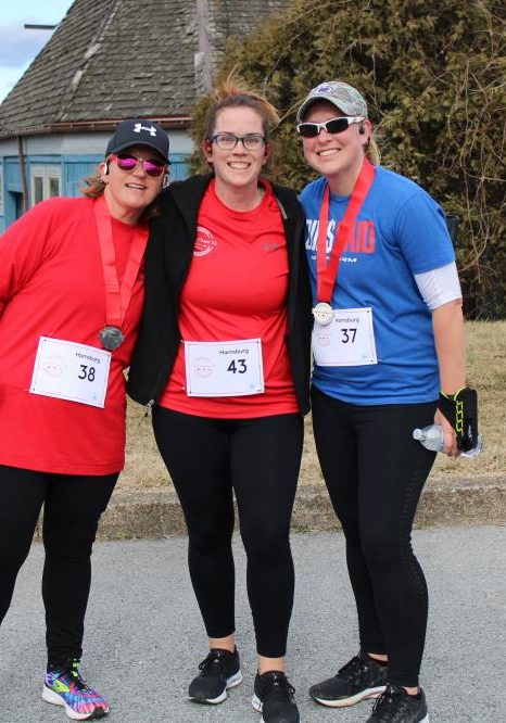 Three people posing after a Cupid's Chase 5k some wearing their medals